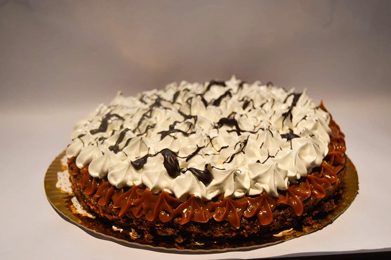 torta brownie con dulce de leche y crema encima, decorada con hilos de chocolate.